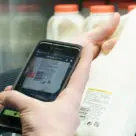 Man uses My Pay Go mobile sefl-checkout on smartphone to scan and pay for milk