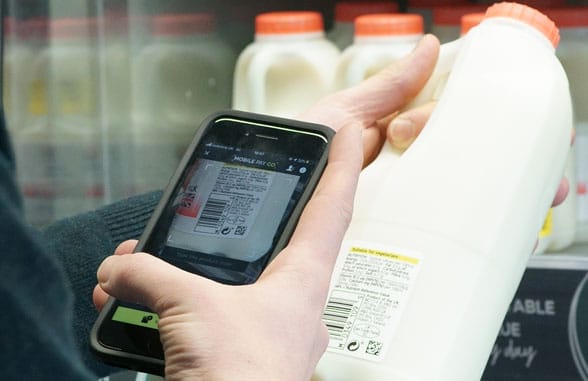 Man uses Mobile Pay Go mobile sefl-checkout on smartphone to scan and pay for milk