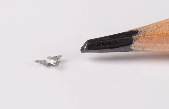 Miniature batteryless flying microchips with NFC next to a pencil tip for scale