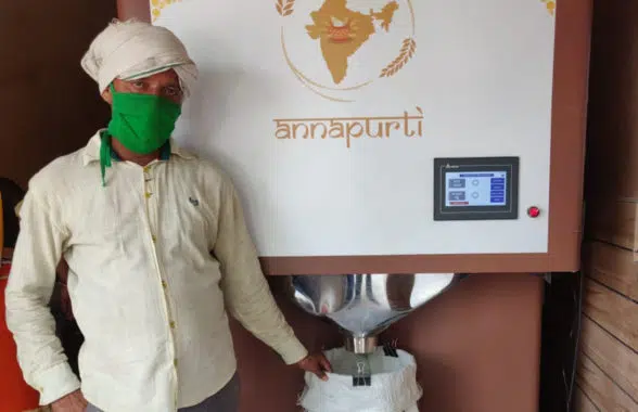 Man standing next to automated biometric commodity dispensers for distributing subsidised food in India