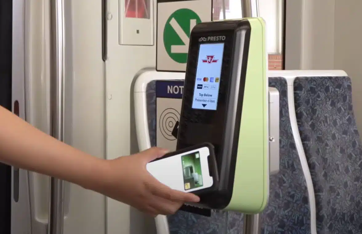 Person using smartphone on a validator on a Toronto bus to make open loop contactless fare payment
